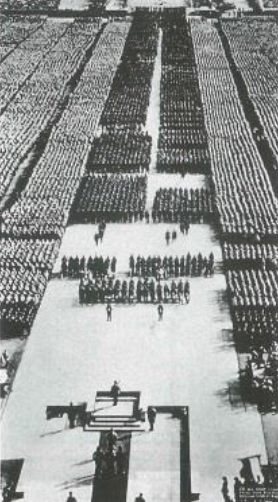 Luftaufnahme einer großen, streng geordneten Menschenmenge bei einer Massenveranstaltung mit Bühne und Rednerpodium